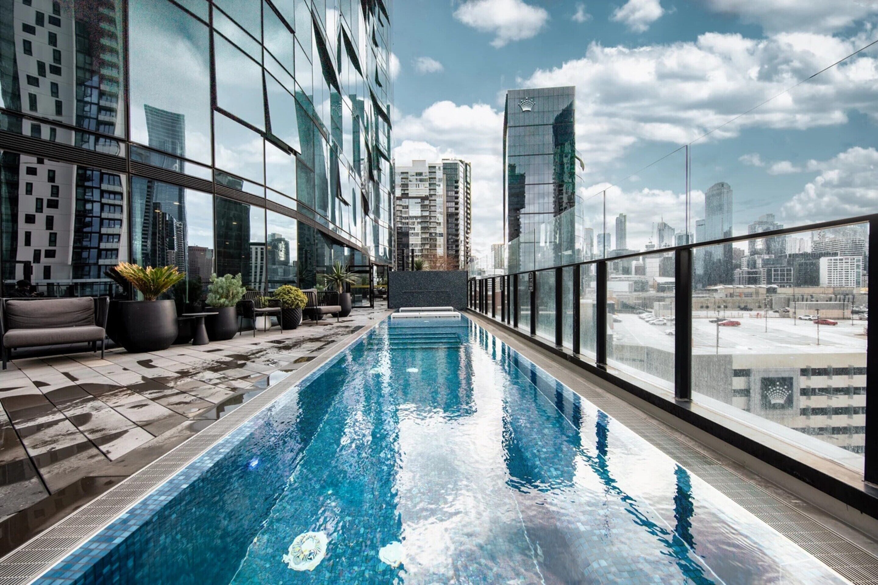 A rooftop pool with a city view, surrounded by modern buildings and potted plants.