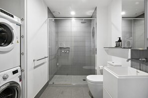 A modern bathroom with a built-in washing machine, a glass-enclosed shower, and a white sink. - Stylish Southbank 1-bed Flat With Luxury Amenities (Melbourne)