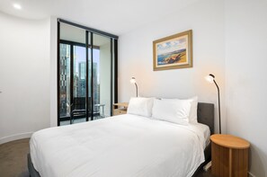 A modern hotel room with a large bed, a view of the city through a glass door, a painting on the wall, and two bedside lamps. - Stylish Southbank 1-bed Flat With Luxury Amenities (Melbourne)