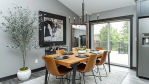A modern dining area with a wooden table set for six, surrounded by leather chairs. A large potted plant is on the left, and a framed artwork hangs above the table. - Spacious 4-bedroom house in peaceful neighborhood 10min from Mayo Clinic. (Rochester)