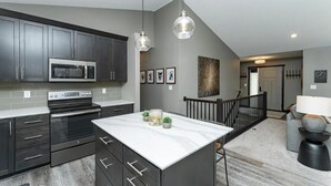 A modern kitchen with dark cabinets, a large island, and pendant lighting. - Spacious 4-bedroom house in peaceful neighborhood 10min from Mayo Clinic. (Rochester)