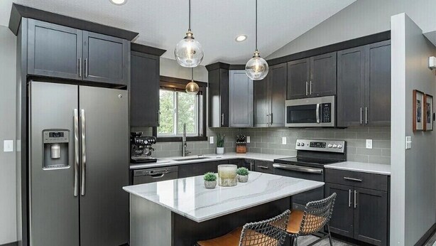 A modern kitchen with dark cabinets, stainless steel appliances, a marble island, and pendant lighting. - Spacious 4-bedroom house in peaceful neighborhood 10min from Mayo Clinic. (Rochester)