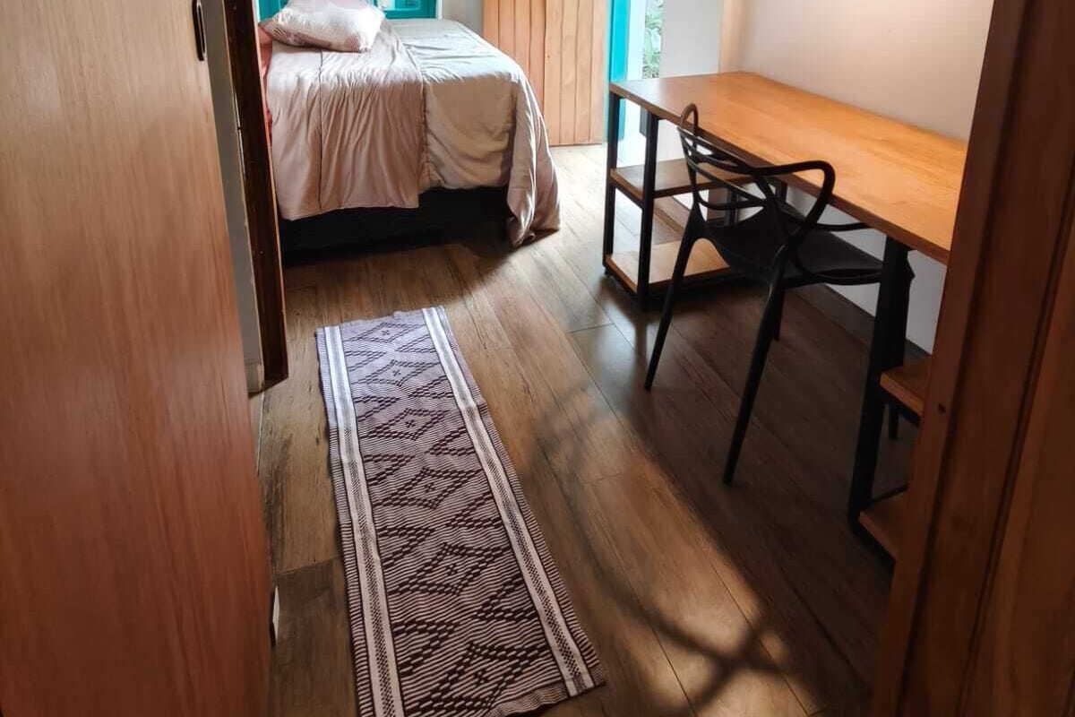 Una habitación con cama, un escritorio de madera, una silla, un tapete estampado y una ventana con contraventanas azules.