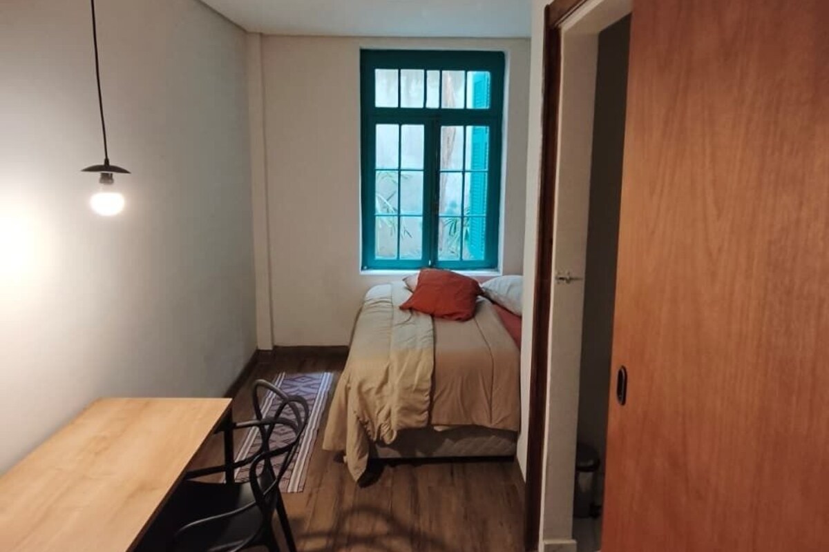Una habitación pequeña con cama, escritorio, silla, ventana y puerta.
