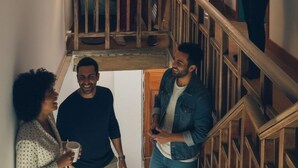 Un interior con varios niveles, barandas de madera, una escalera y un grupo de personas en el nivel superior.