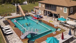 A swimming pool with a slide, lounge chairs, and a building with a balcony.