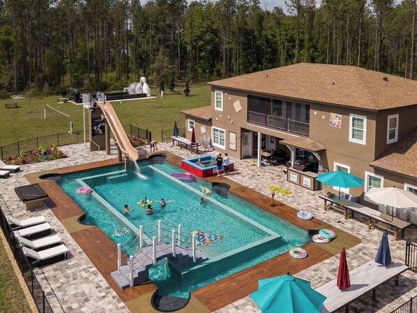 Une piscine avec un toboggan, des chaises longues et un bâtiment doté d’un balcon.