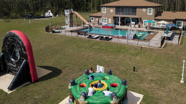 A pool area with a slide, inflatable play structures, and a house in the background.