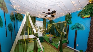Una habitación con dos literas, un ventilador de techo, luces colgantes y decoración de paredes con motivos forestales.