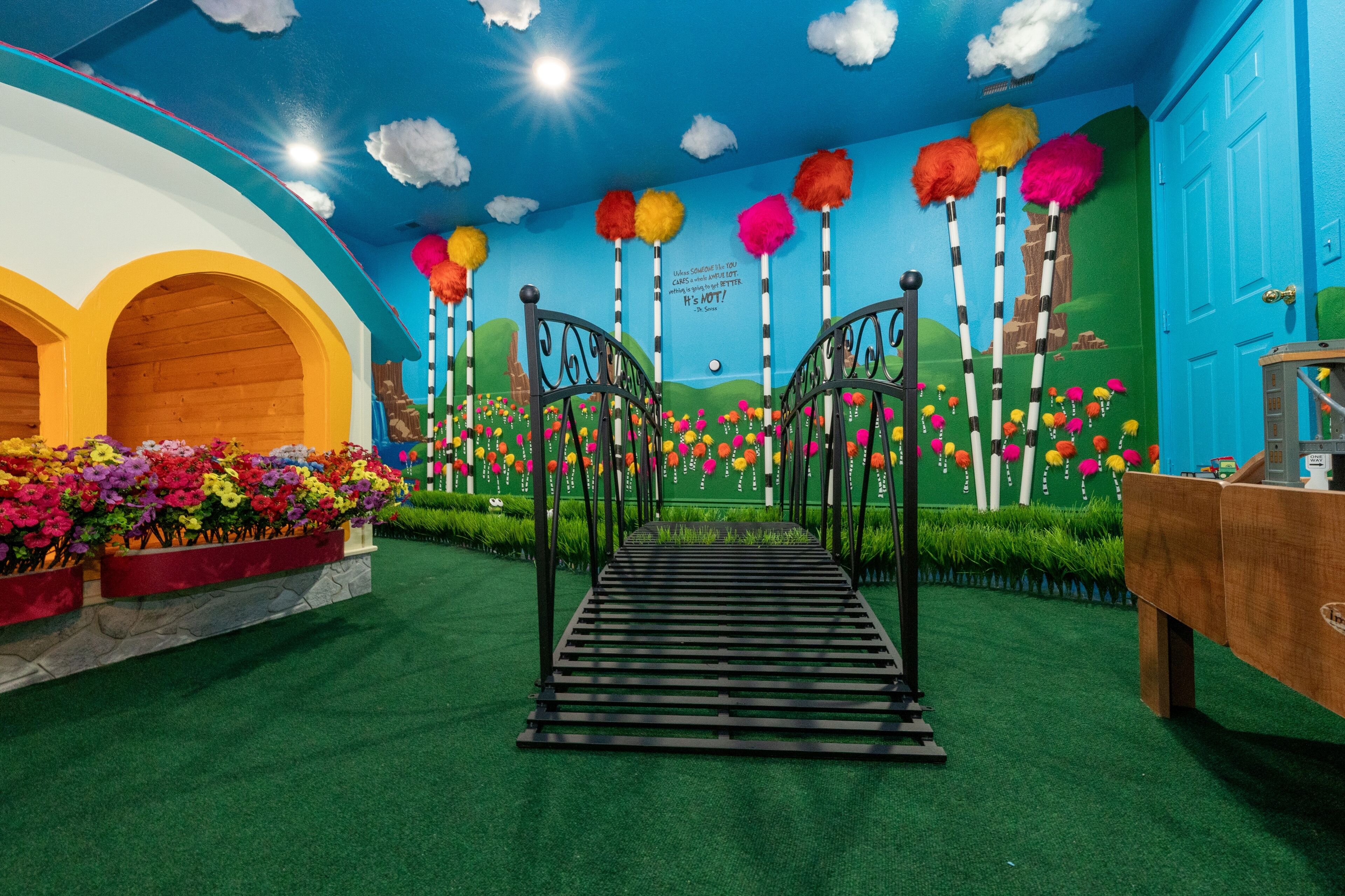 A colorful indoor garden with a pathway, artificial flowers, and a mural on the wall.