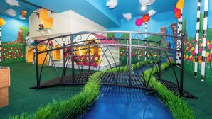 Zona de juegos con un puente sobre una piscina azul, rodeada de murales coloridos y césped artificial.