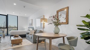 Un salon moderne avec une table ronde en bois, un canapé gris, une grande fenêtre donnant sur un beau paysage et un miroir accroché au mur.