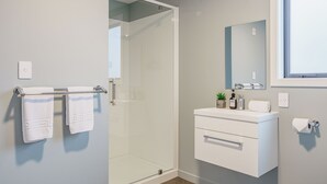 A modern bathroom with a glass shower enclosure, a white vanity with a mirror, and a towel rack with two towels. - Woolshed Suites (Lake Tekapo)