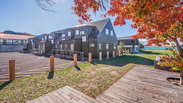 A modern building with multiple units, a parking area, and a grassy landscape with a wooden deck. - Woolshed Suites (Lake Tekapo)