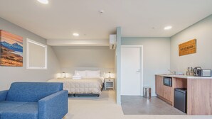 A bedroom with a bed, bedside table, lamp, and a blue armchair. - Woolshed Suites (Lake Tekapo)