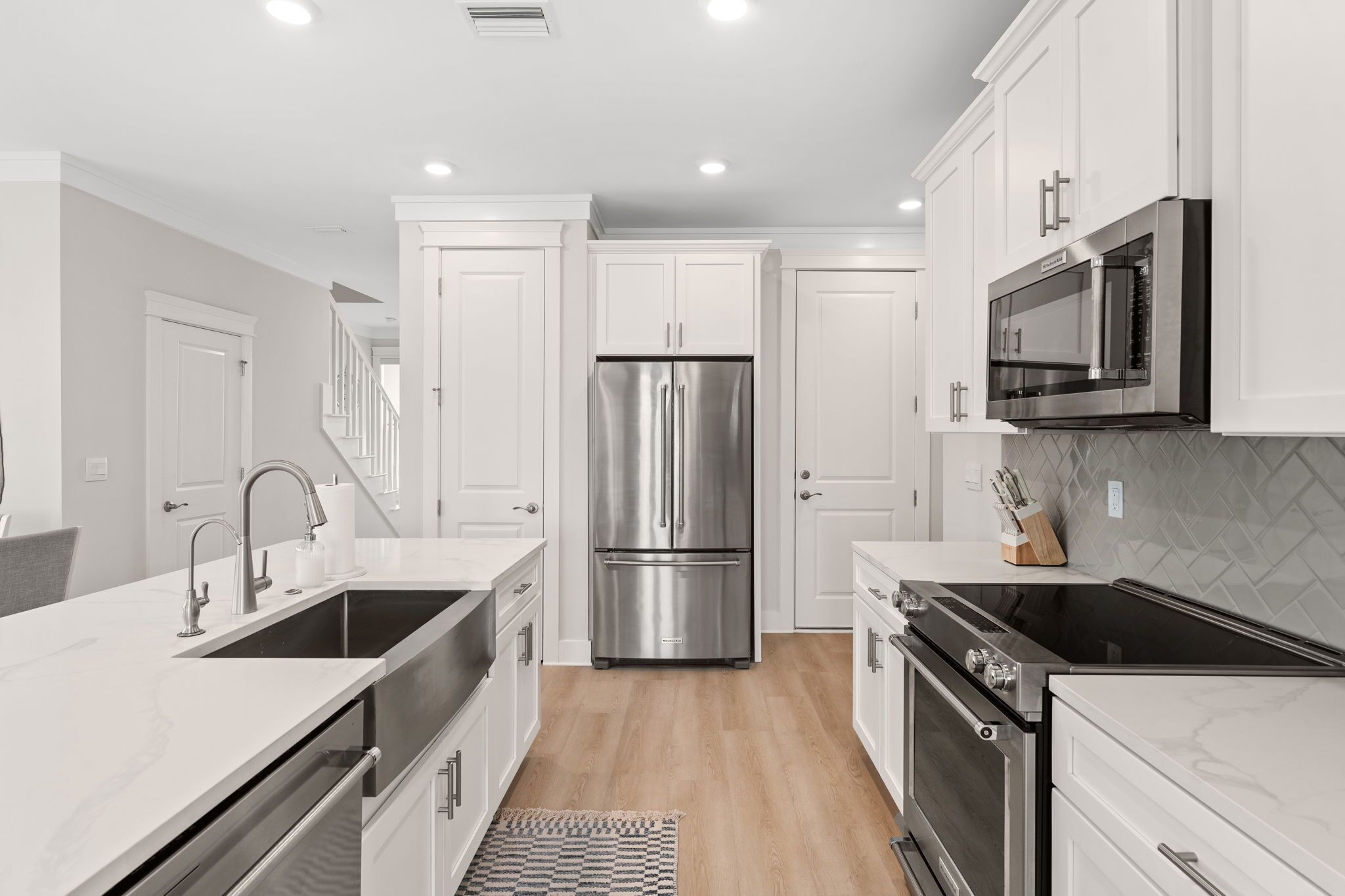 A modern kitchen with white cabinetry, stainless steel appliances, and a marble countertop.