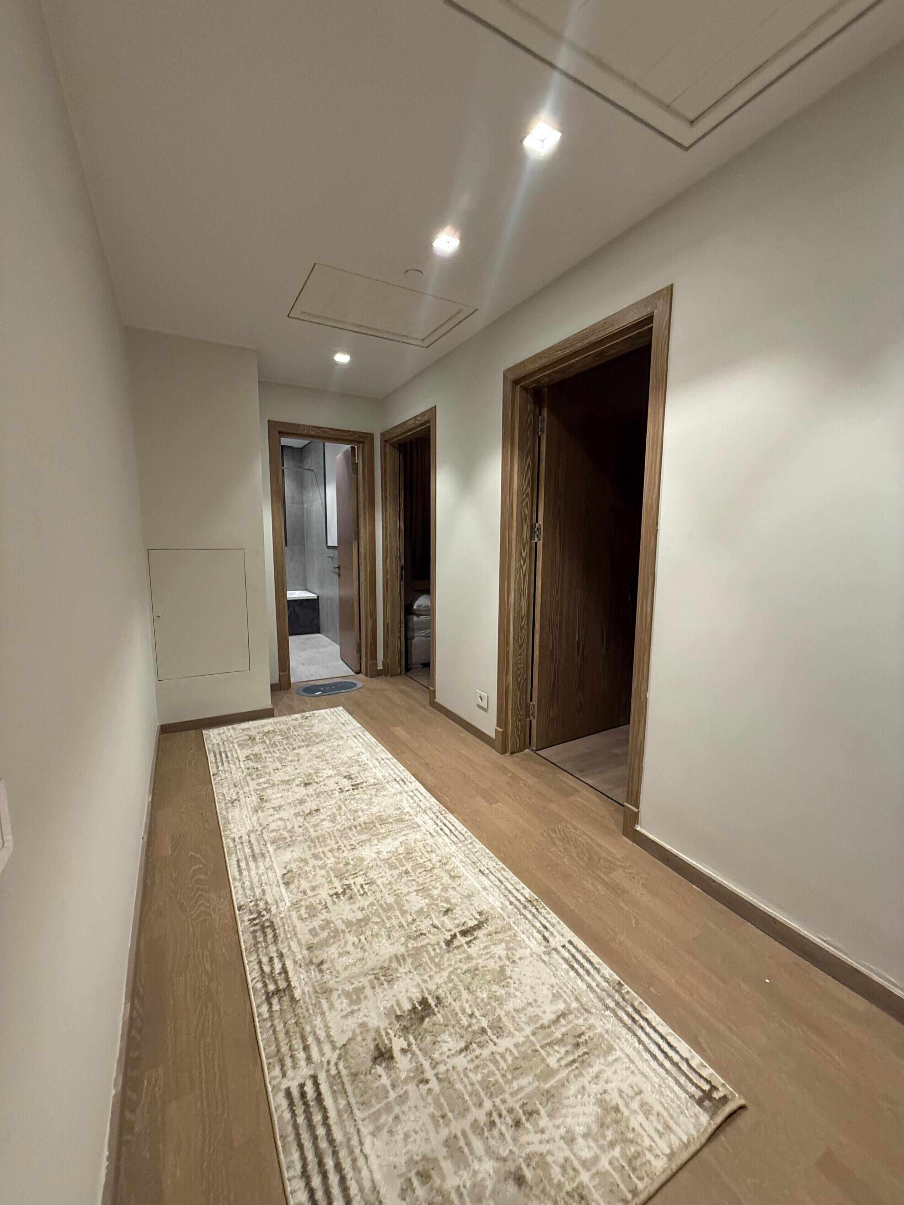 A hallway with wooden flooring, a patterned rug, and doors leading to other rooms.