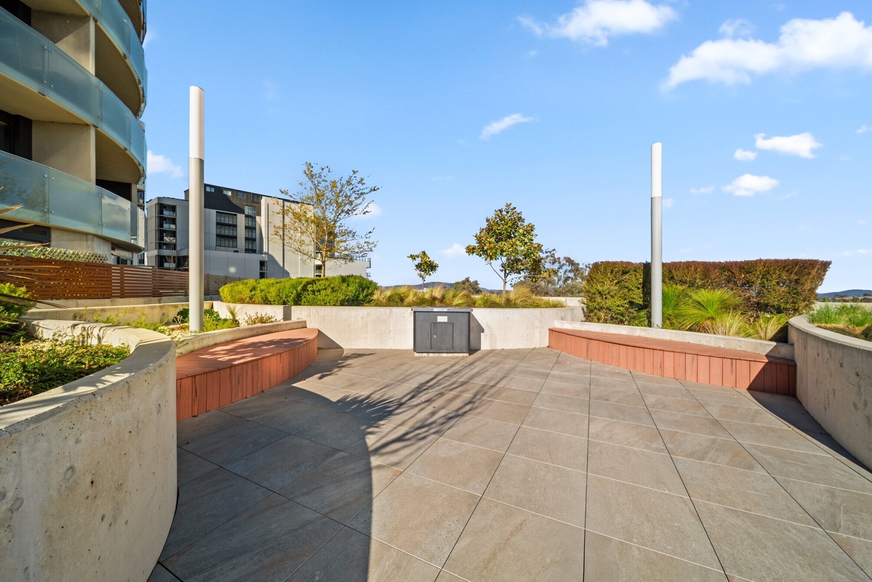 Een terras buiten met een vloer van gebogen beton, omringd door lage muren en groen.