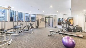 Une salle de sport spacieuse, dotée de divers appareils d’exercice, de grandes fenêtres et d’un sol décoré d’un motif en chevrons.
