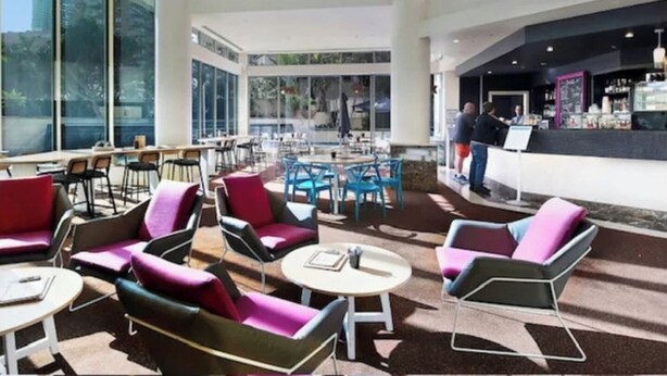 Un vaste espace extérieur aménagé avec des chaises et des tables modernes, de grandes fenêtres offrant une vue sur la ville et un bar avec un comptoir.
