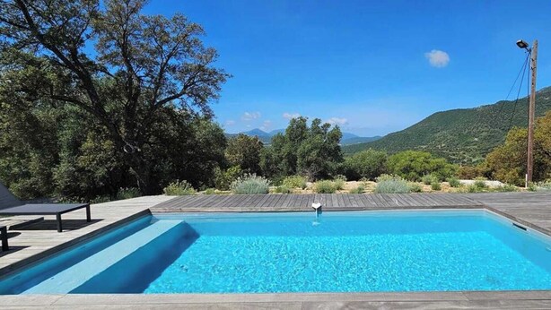 A rectangular swimming pool with a wooden deck and lounge chairs on either side.