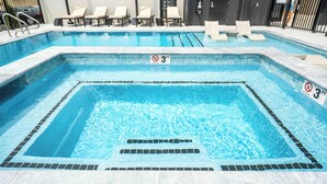A swimming pool with a 3 FT no diving sign, lounge chairs, and a tiled deck.