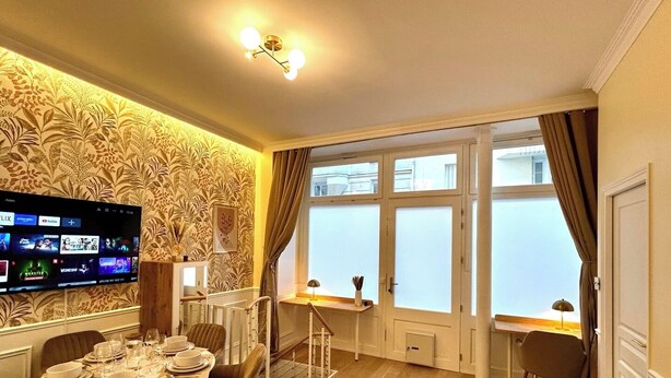 Una sala de estar moderna con comedor, ventanas amplias con vidrio esmerilado, un televisor de pantalla plana en la pared y una zona de estar acogedora con un sofá.