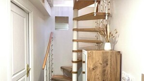 Una escalera con escalones de madera y barandilla blanca, que conduce a una plataforma con un armario de madera y un jarrón con plantas secas.
