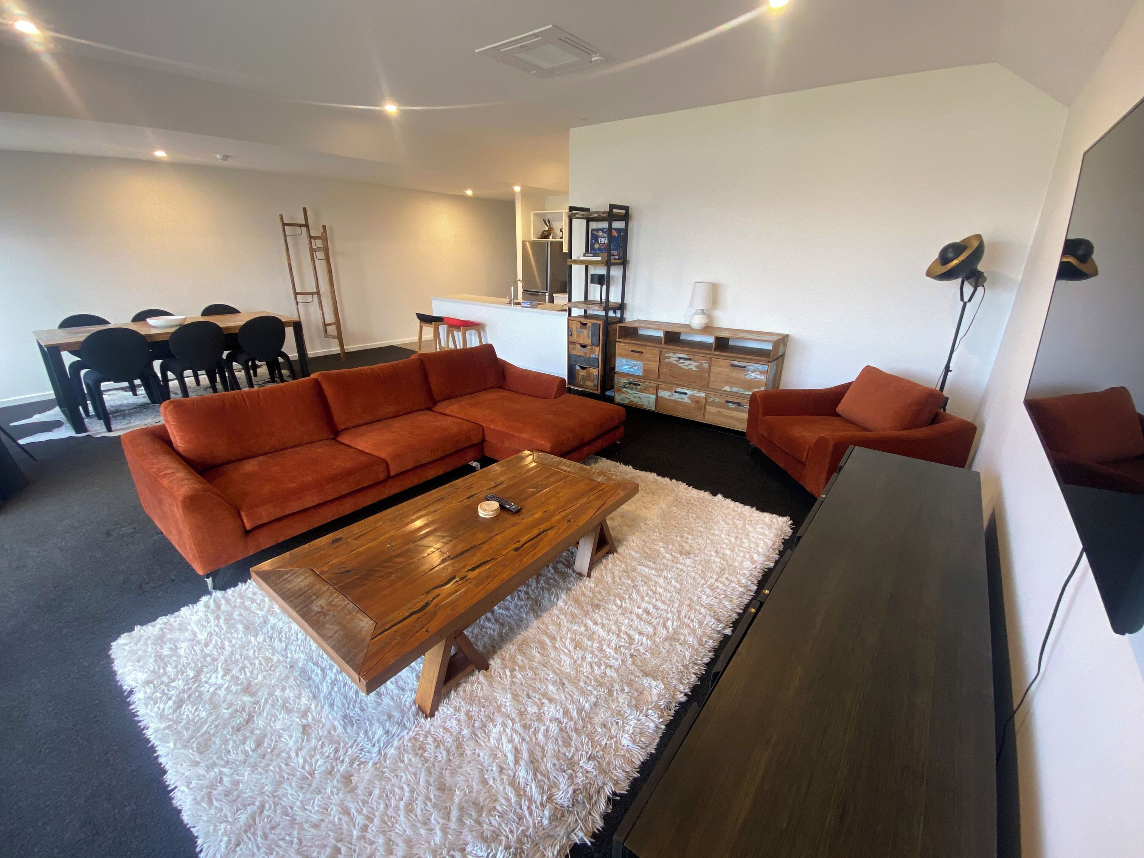 Un salon moderne avec un canapé d’angle, une table basse en bois, un tapis à poils longs blanc et un buffet en bois foncé.