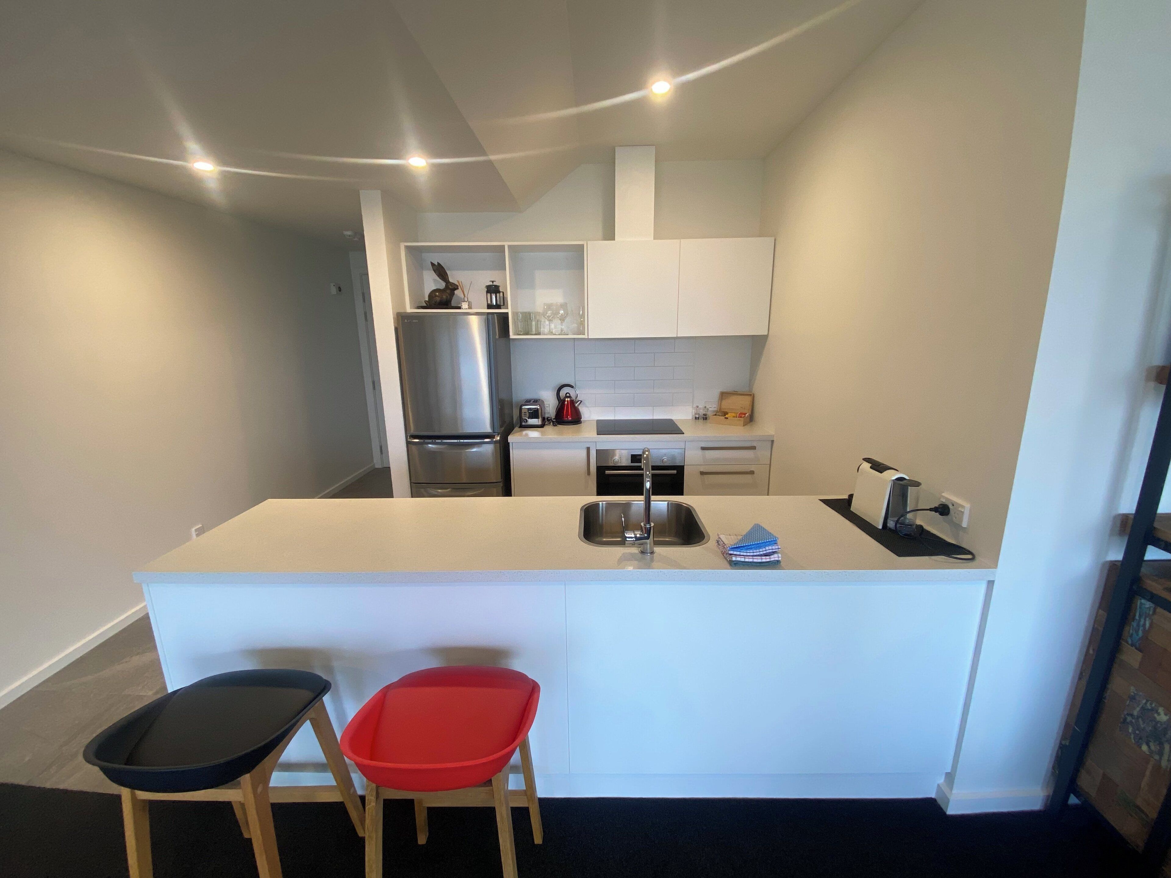 Una cocina compacta con una isla central, un refrigerador y un lavamanos. Hay dos taburetes y una tostadora en la isla.
