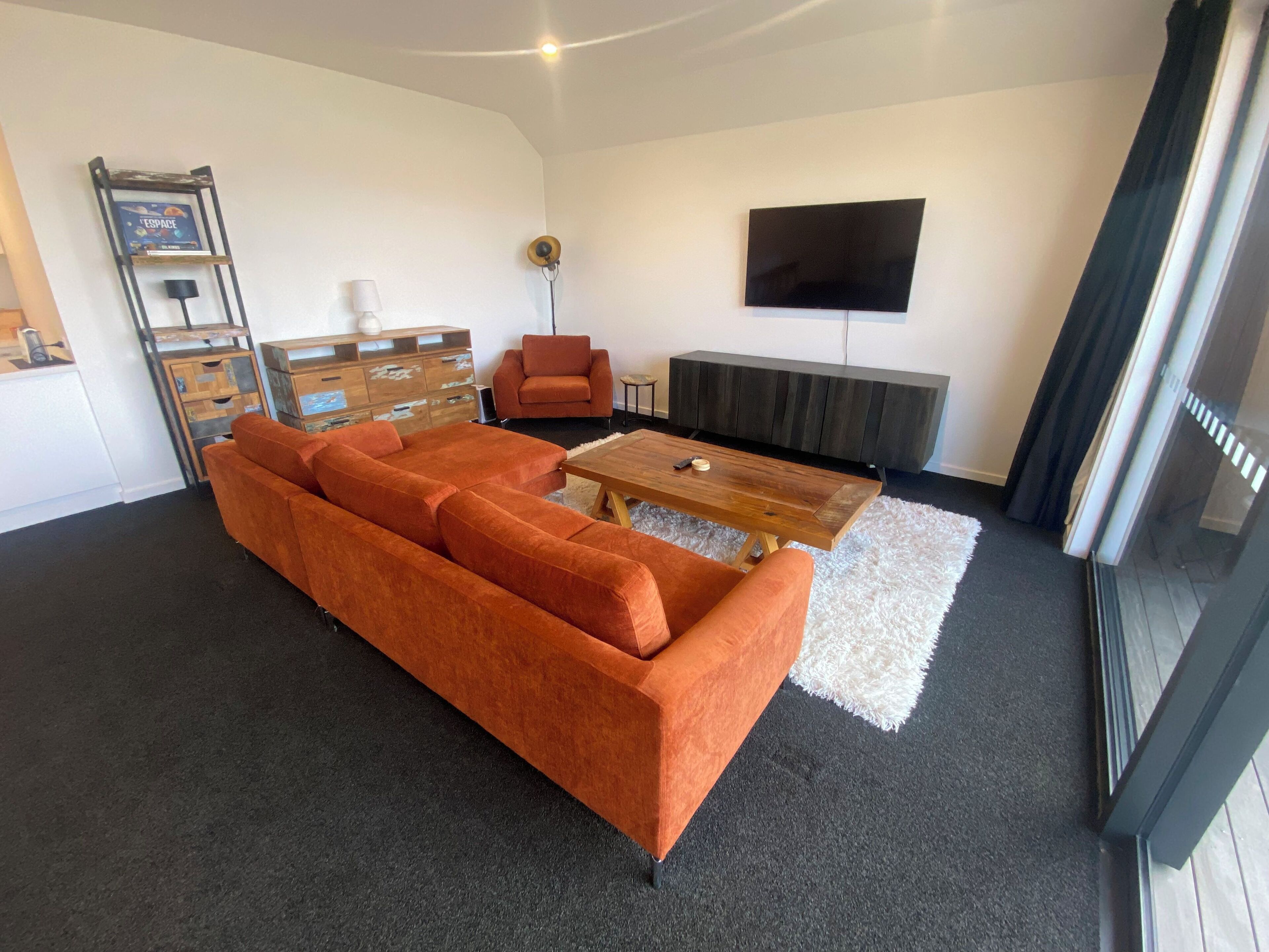 A modern living room with a sectional sofa, a wooden coffee table, a TV mounted on the wall, and a fireplace.