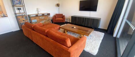 A modern living room with a sectional sofa, a wooden coffee table, a TV mounted on the wall, and a fireplace.