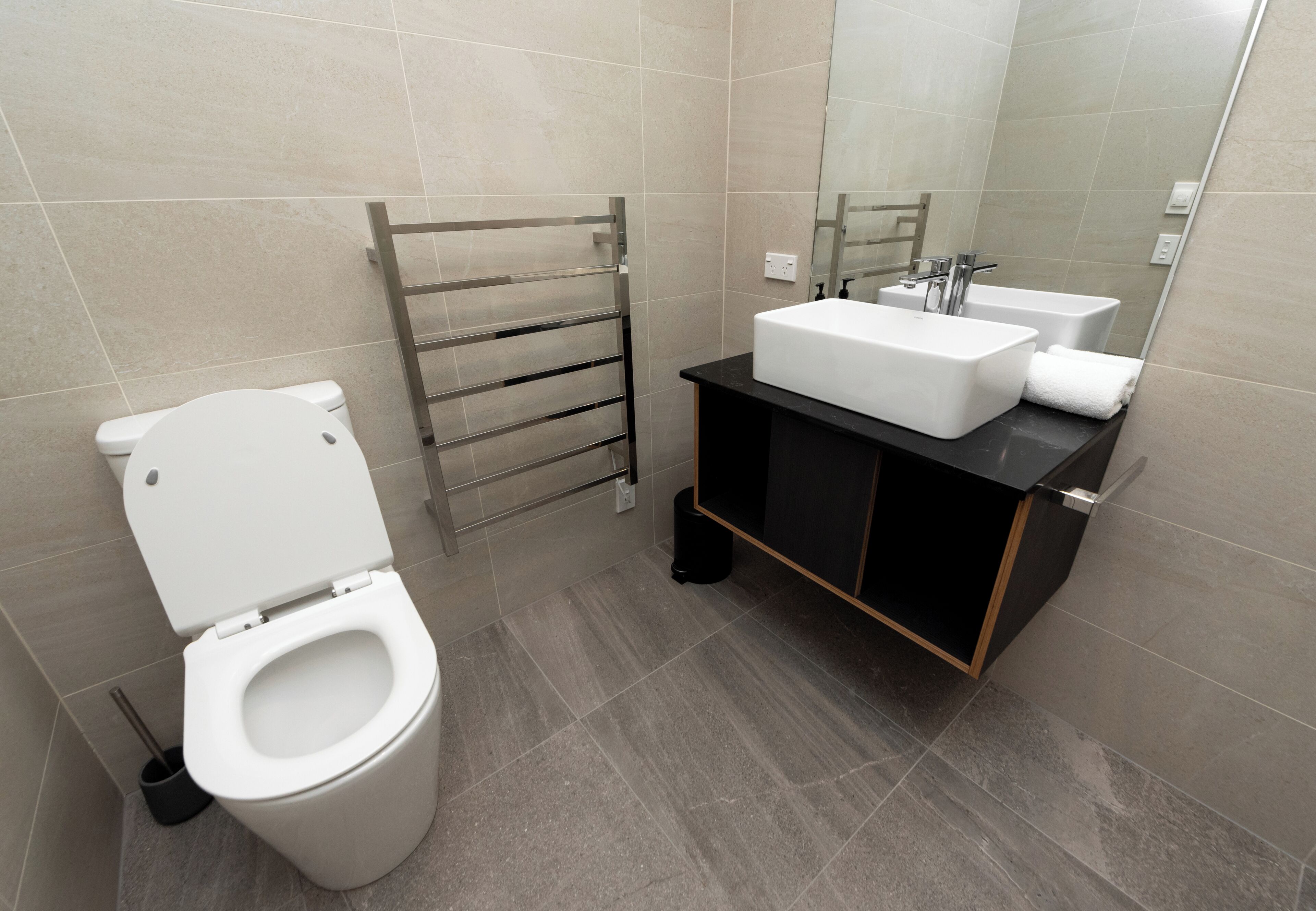 Un baño moderno con inodoro blanco, toallero y lavabo con espejo.