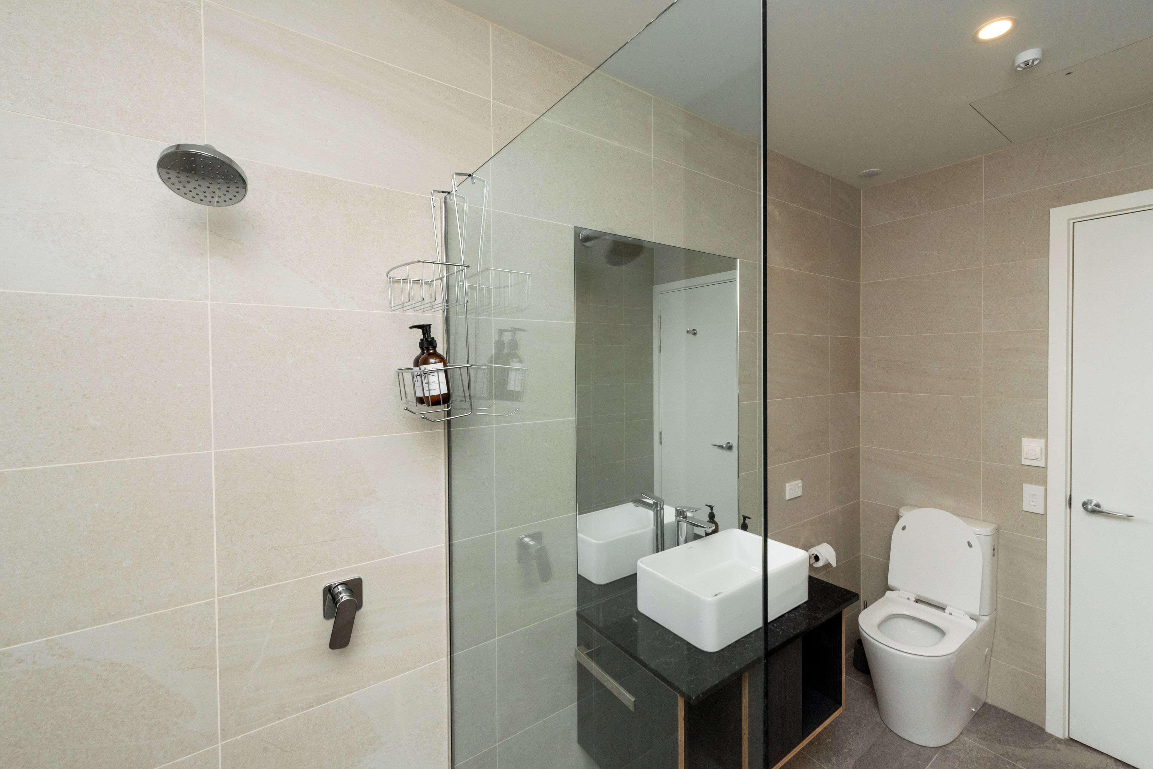Ein modernes Badezimmer mit Duschkabine aus Glas, zwei Waschbecken und einer Toilette.