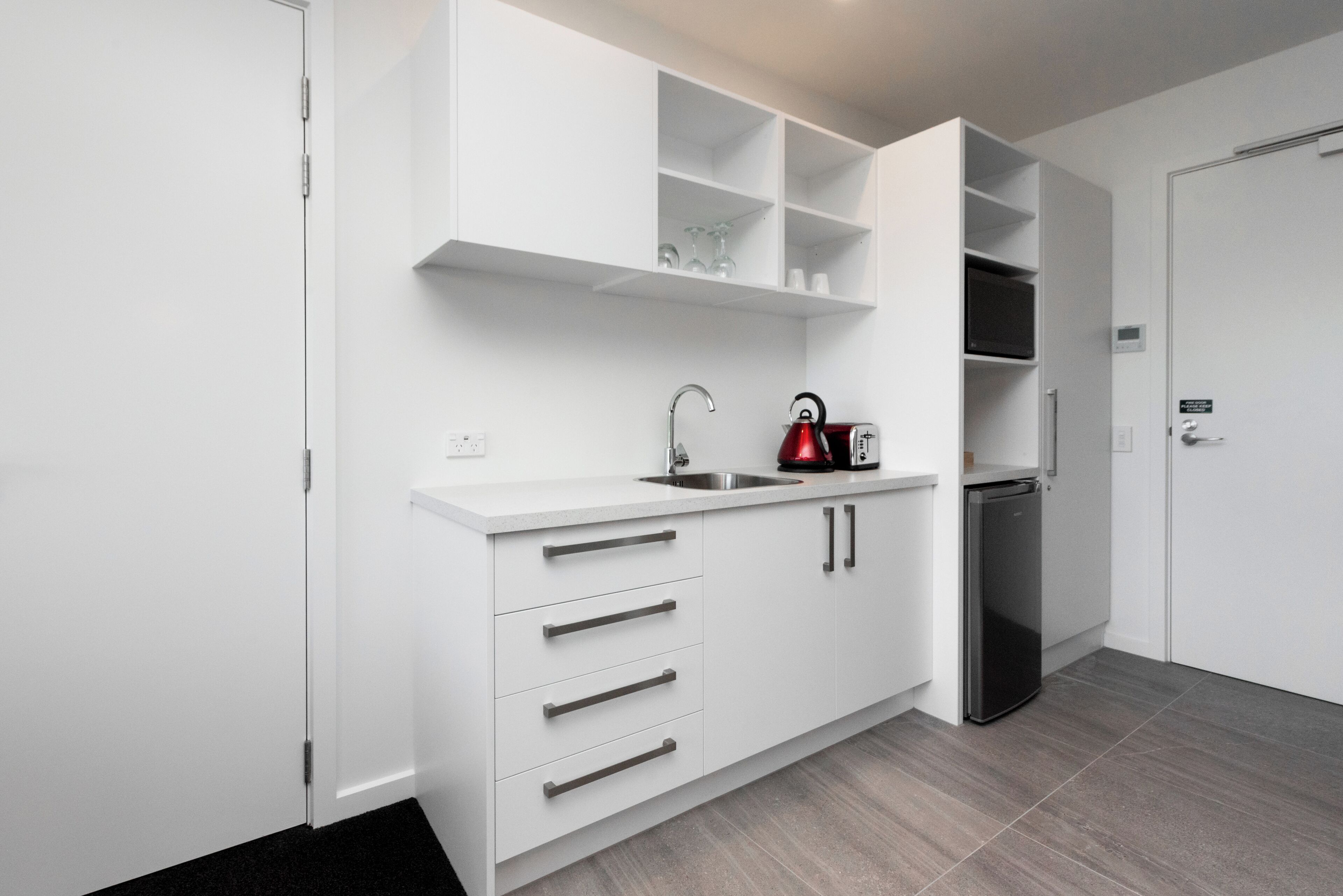 A modern kitchen with white cabinetry, a stainless steel sink, a red kettle, and a built-in microwave.