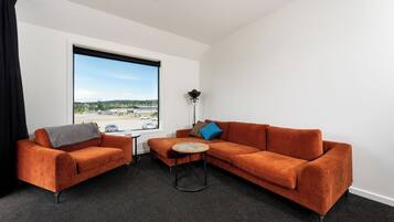 A modern room with a large window, a sofa, a small table, and a lamp.