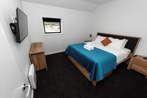 A modern bedroom with a bed, a TV mounted on the wall, a window with a view, and a small wooden nightstand.