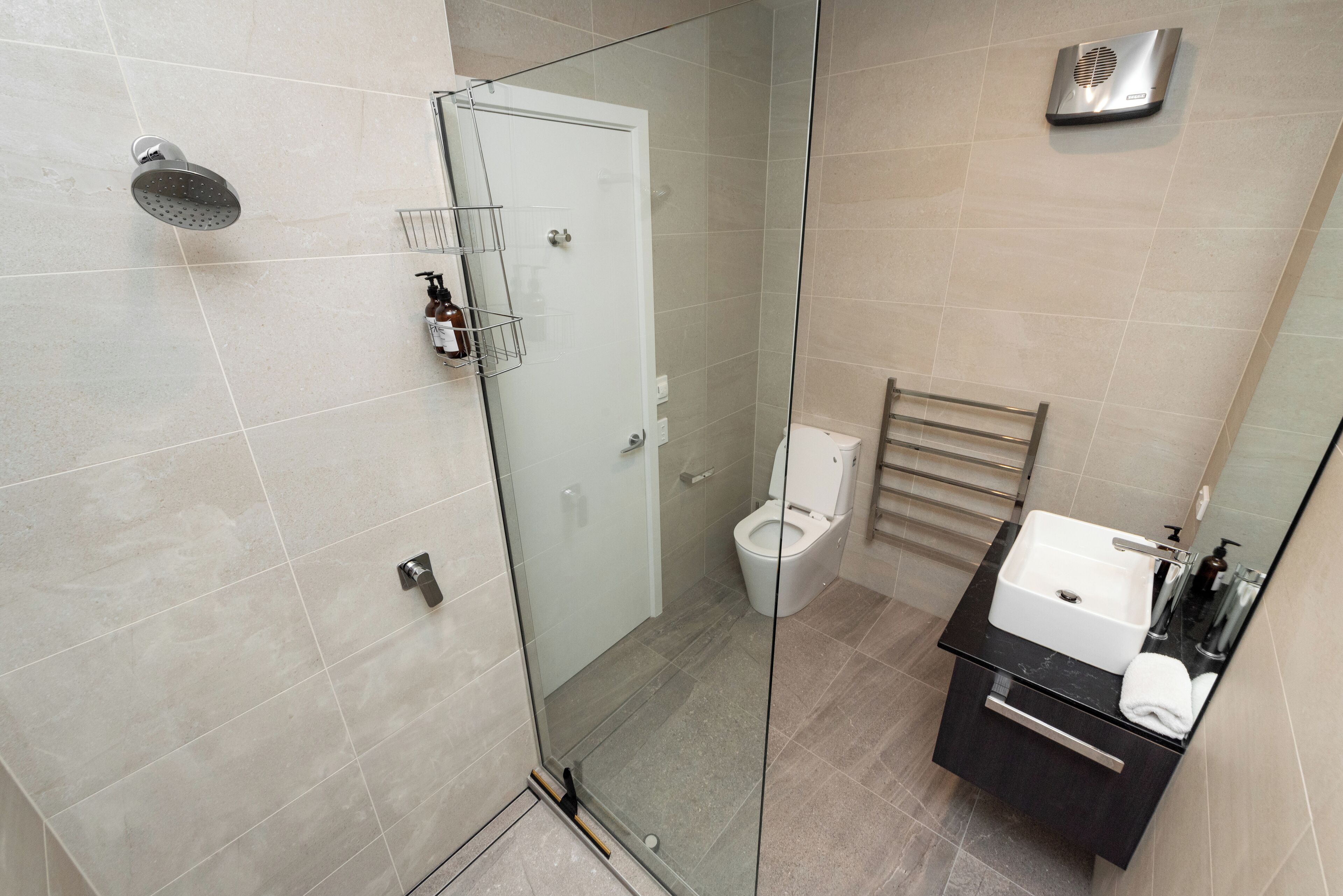 A modern bathroom with a glass-enclosed shower, a toilet, and a sink with a towel.