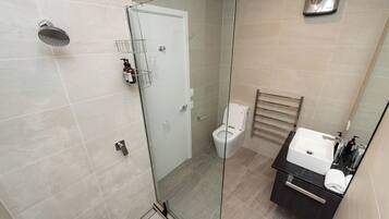 A modern bathroom with a glass-enclosed shower, a toilet, and a sink with a towel.