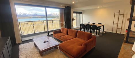 Amplia sala de estar con un gran ventanal que ofrece vistas a la montaña, un sofá marrón, una mesa de centro de madera y un comedor con mesa y sillas.