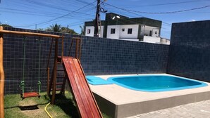 Um quintal com piscina, balanço de madeira e um pátio de tijolos.