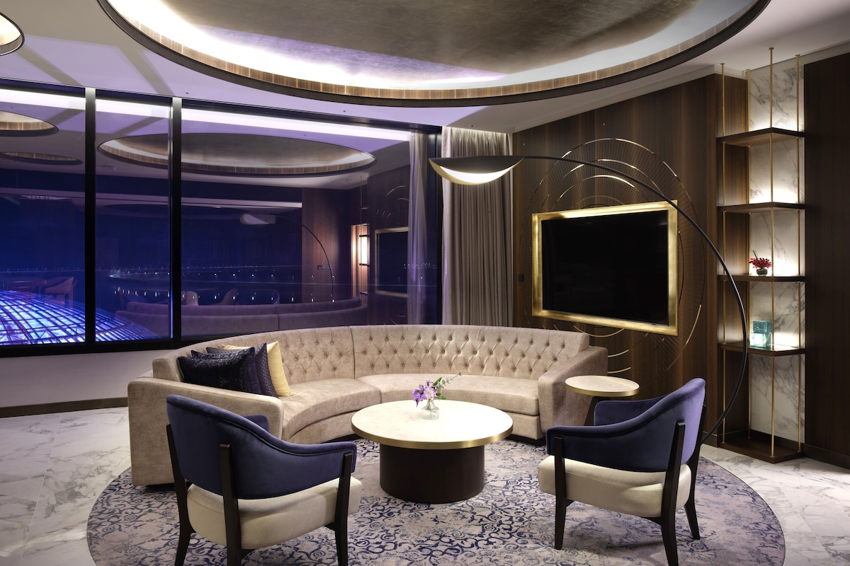 A modern living room with a curved sectional sofa, two armchairs, a round coffee table, and a large flat-screen TV.