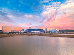 A large stadium with 'INSPIR' branding, surrounded by modern buildings and a body of water. - Inspire Entertainment Resort (Incheon)