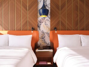 A hotel room with two beds, a nightstand with a lamp, and a patterned wallpaper.