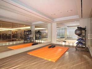 A gym with exercise equipment, orange mats, and a large mirror.