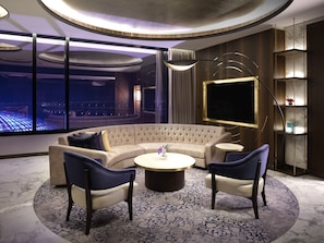 A modern living room with a curved sectional sofa, two armchairs, a round coffee table, and a large flat-screen TV. - Inspire Entertainment Resort (Incheon)
