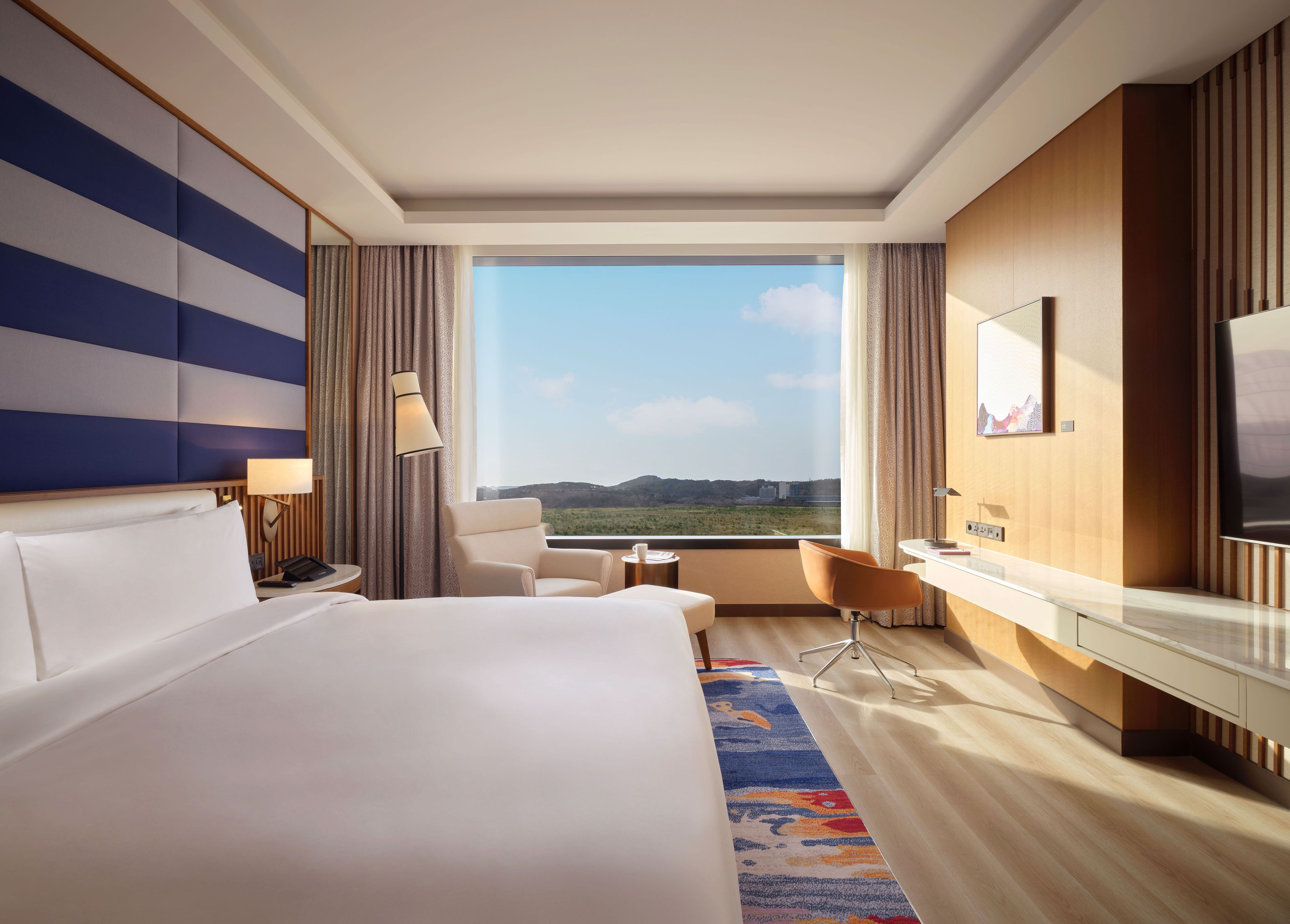 A hotel room with a large bed, a desk, a chair, and a view of the outdoors.