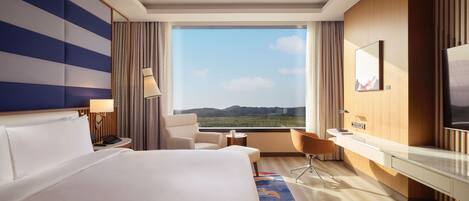 A hotel room with a large bed, a desk, a chair, and a view of the outdoors.