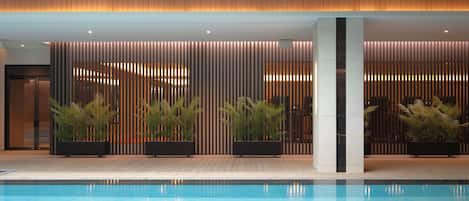 Un área de piscina interior moderna con techo de madera, listones verticales y plantas en macetas.