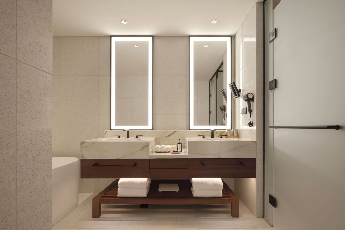 Un baño moderno con dos lavamanos, un espejo grande y un banco con toallas.